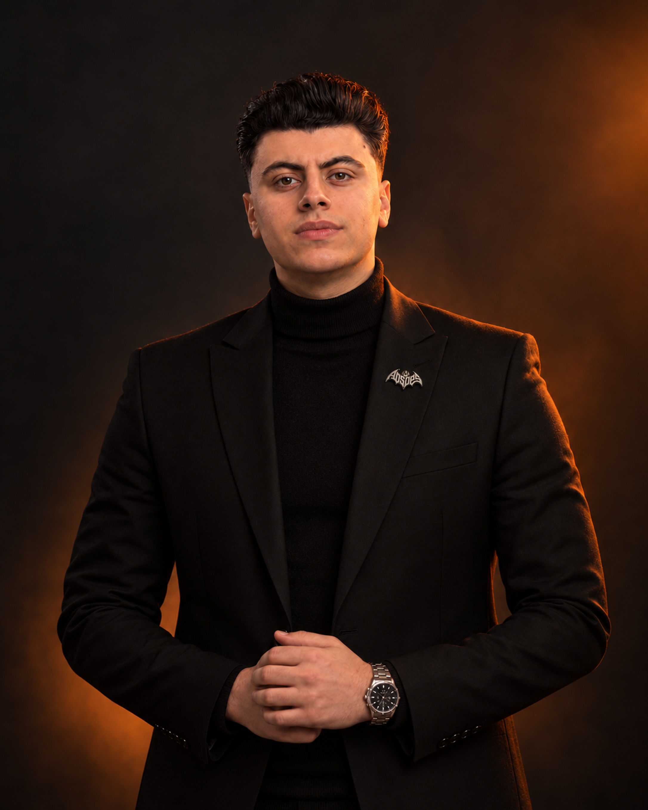 Ibrahem Khaled in a black overcoat over a black turtleneck, hands clasped.