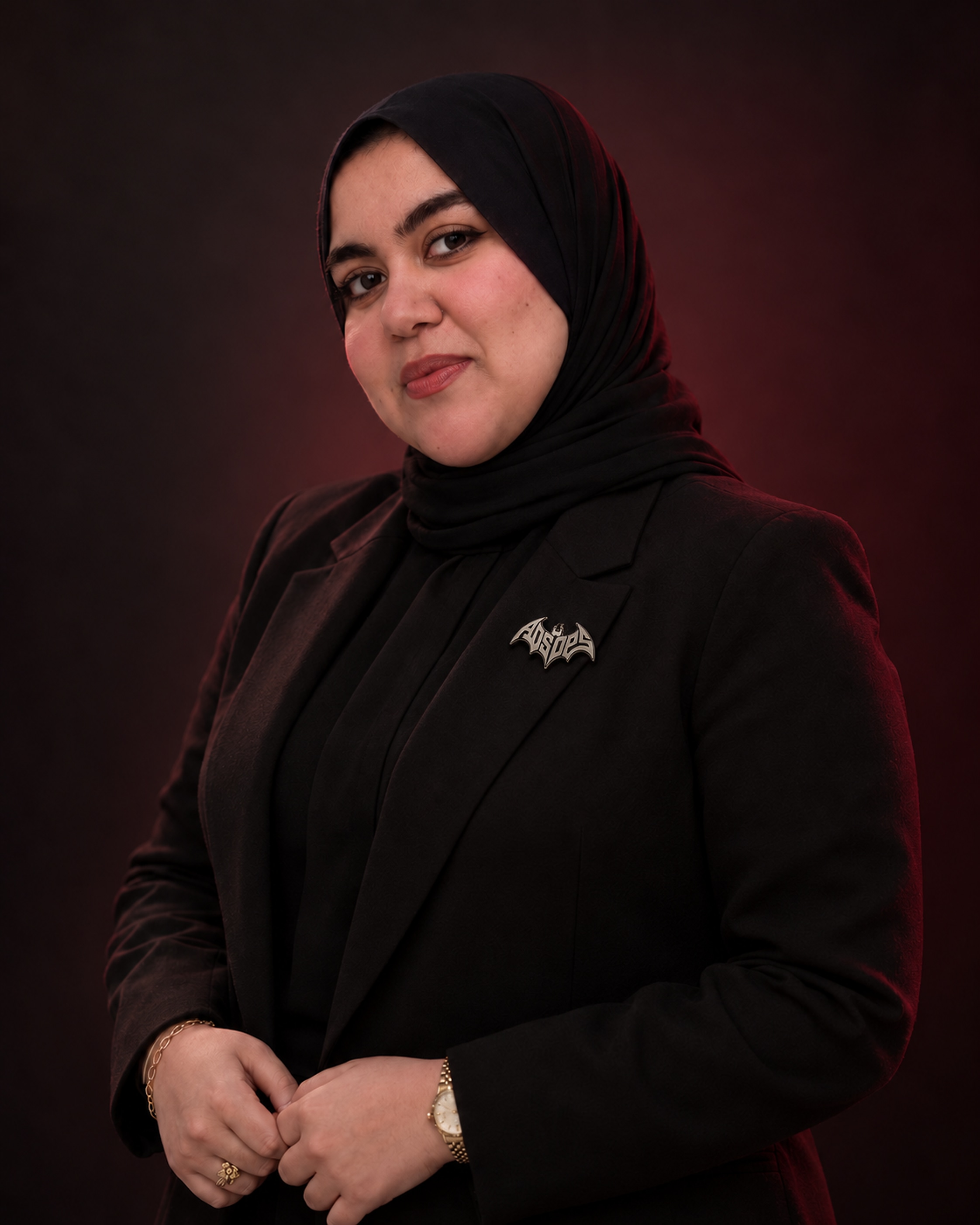 Rana Zawal in black tailoring and a black hijab, against a dark background.